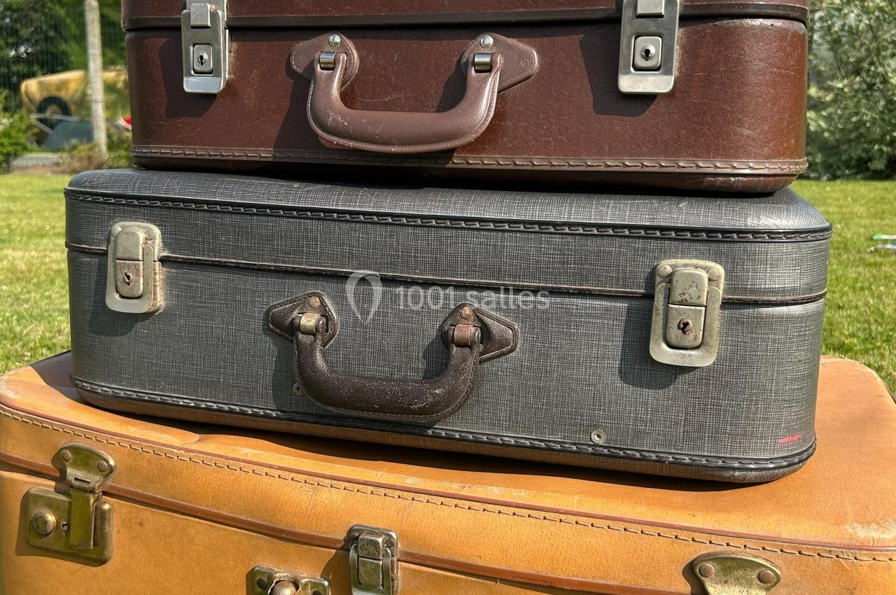 Trois valises vintage empilées, en cuir et tissu, posées sur une surface en extérieur avec de l'herbe en arrière-plan.