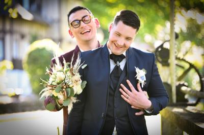 Un couple en tenue de mariage s'embrasse dans un champ de blé, tenant des ballons colorés sous un ciel bleu.