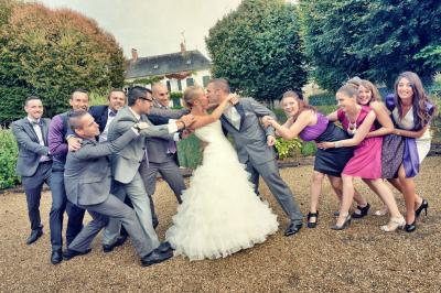 Un couple en tenue de mariage s'embrasse dans un champ de blé, tenant des ballons colorés sous un ciel bleu.
