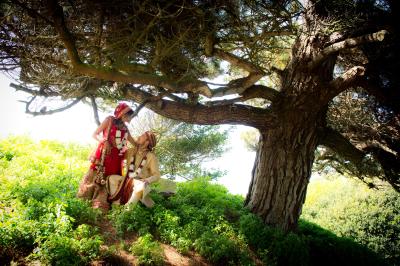 Un couple en tenue de mariage s'embrasse dans un champ de blé, tenant des ballons colorés sous un ciel bleu.