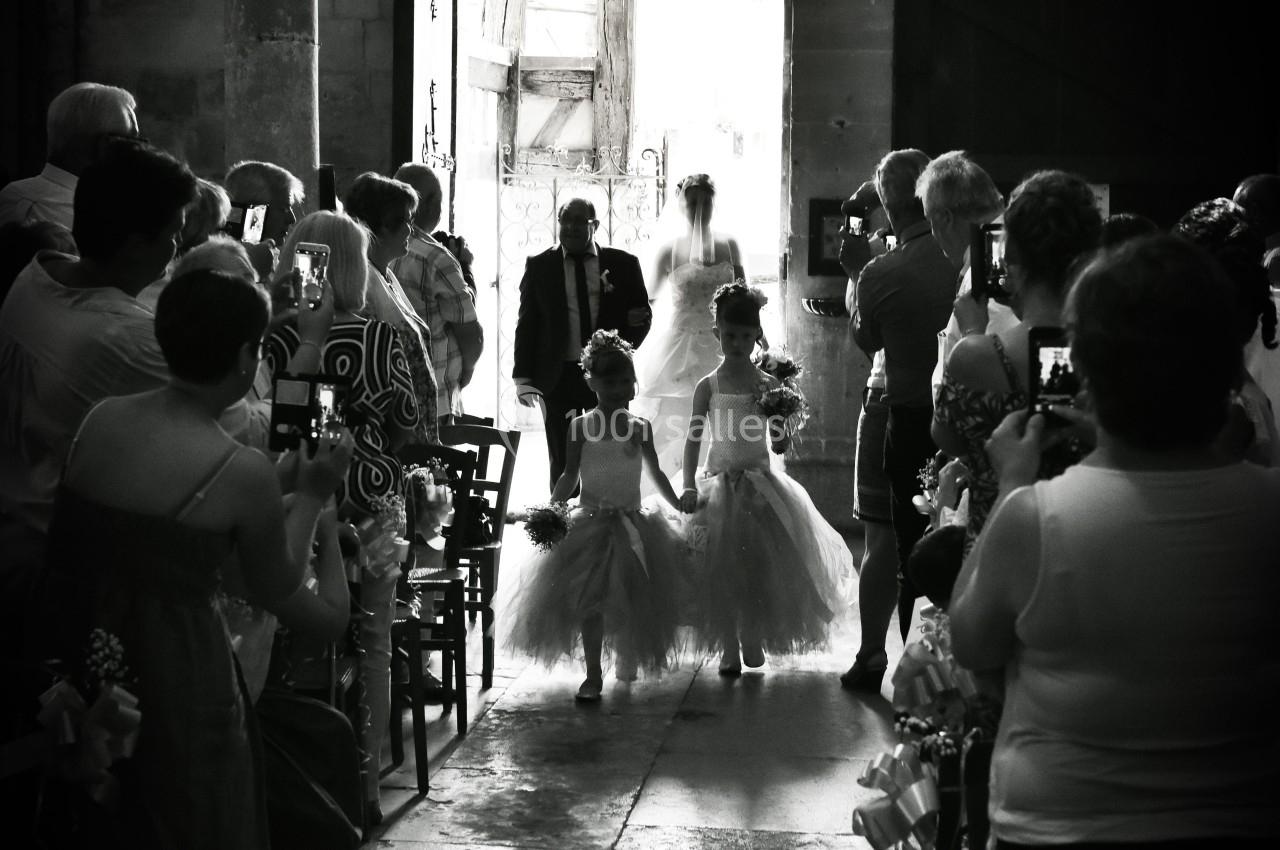 Deux enfants en tenue élégante marchent dans une allée d'église, suivis par une mariée et un homme, sous le regard des…