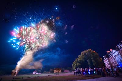 Un couple en tenue de mariage s'embrasse dans un champ de blé, tenant des ballons colorés sous un ciel bleu.