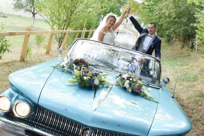 Un couple en tenue de mariage s'embrasse dans un champ de blé, tenant des ballons colorés sous un ciel bleu.