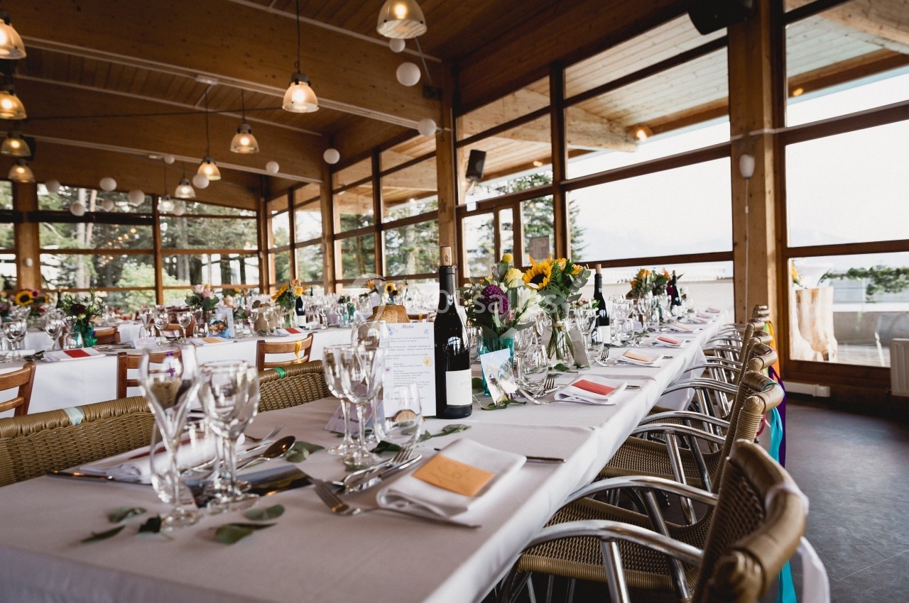 Salle de réception lumineuse avec de longues tables dressées, décorées de fleurs et de verres élégants.