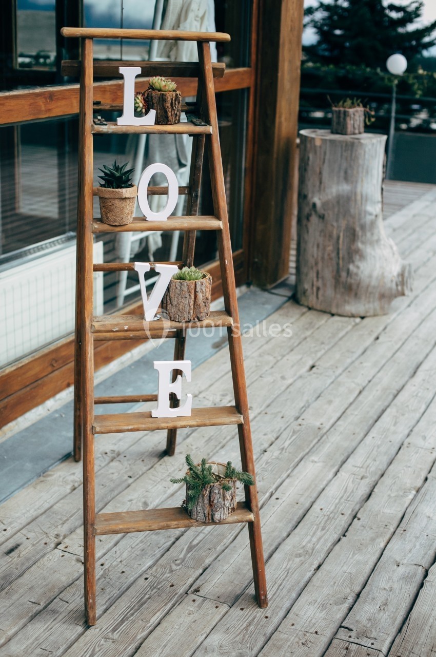 Échelle en bois décorée de plantes en pots et de lettres formant le mot ’LOVE’, posée sur une terrasse en bois.