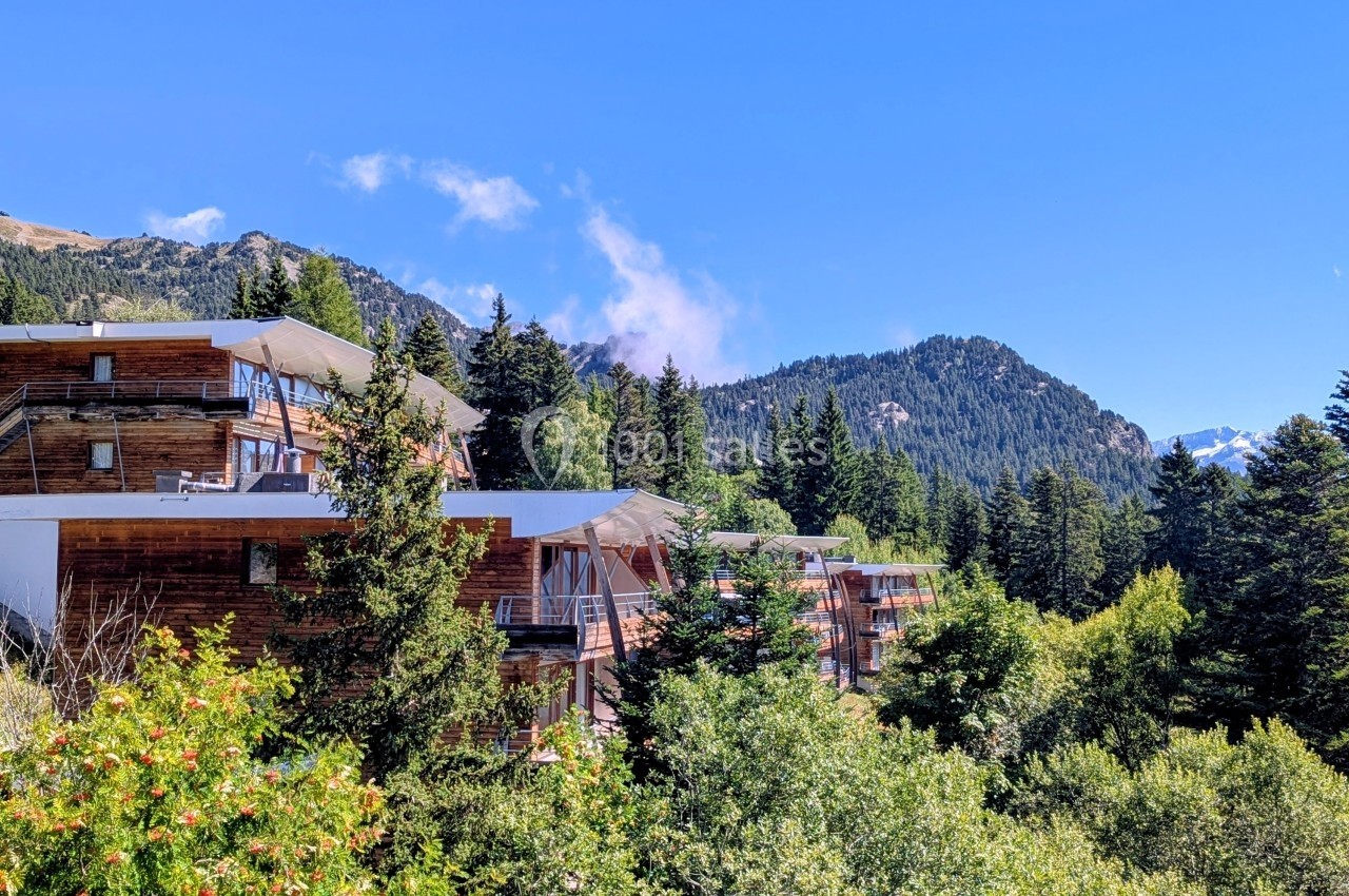 Chalets en bois entourés de forêts et montagnes sous un ciel bleu clair.