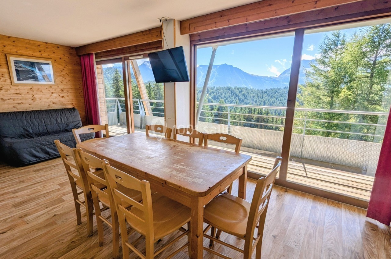 Salle à manger lumineuse avec table en bois, chaises assorties, canapé et grande baie vitrée offrant une vue sur les…