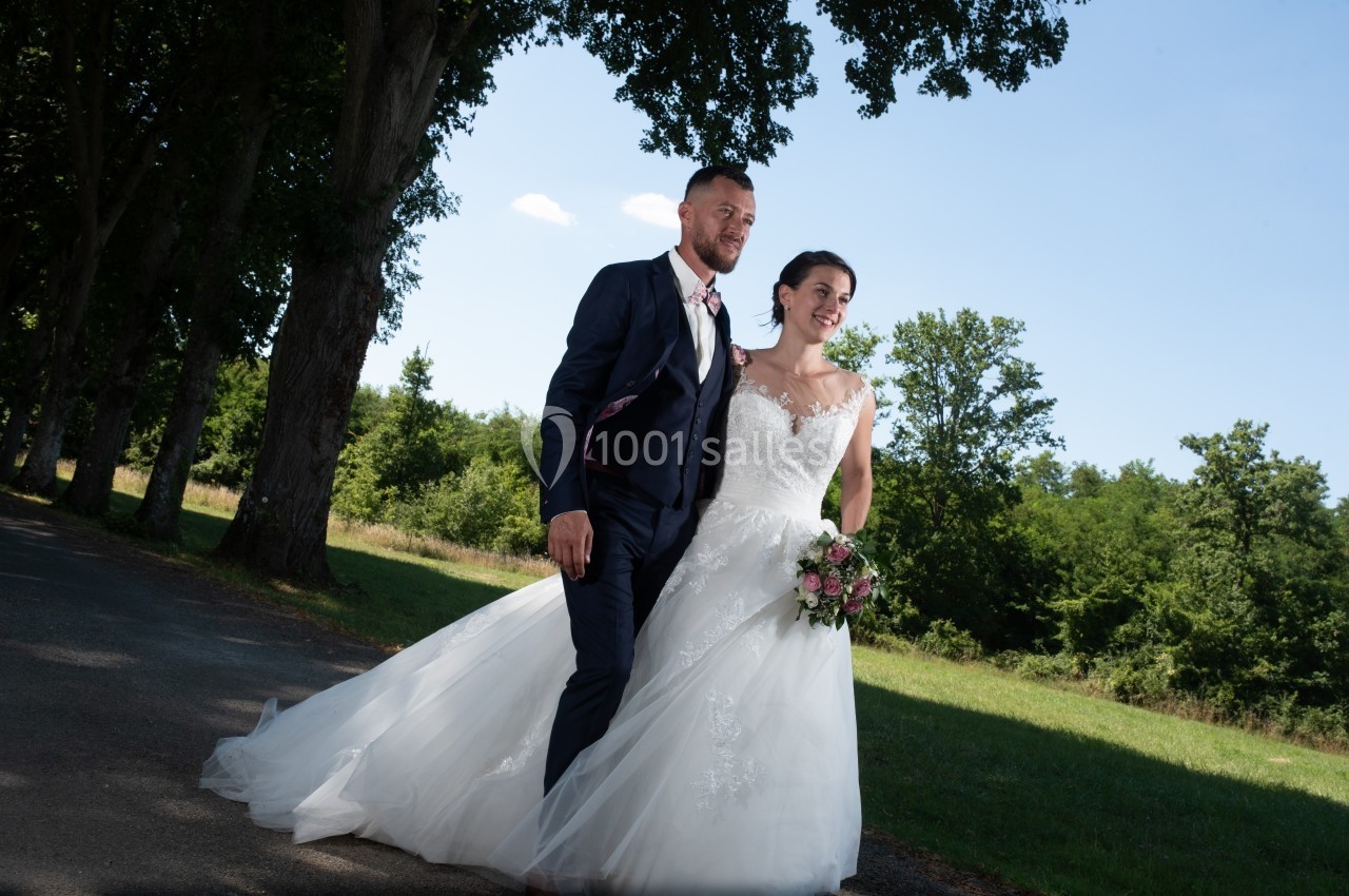 Un couple de mariés marchant sur une route bordée d'arbres par une journée ensoleillée.