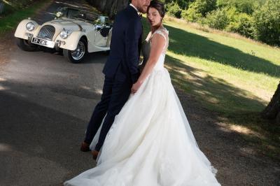 Voiture ancienne décapotable décorée de fleurs pour une cérémonie, stationnée sur une rue pavée.