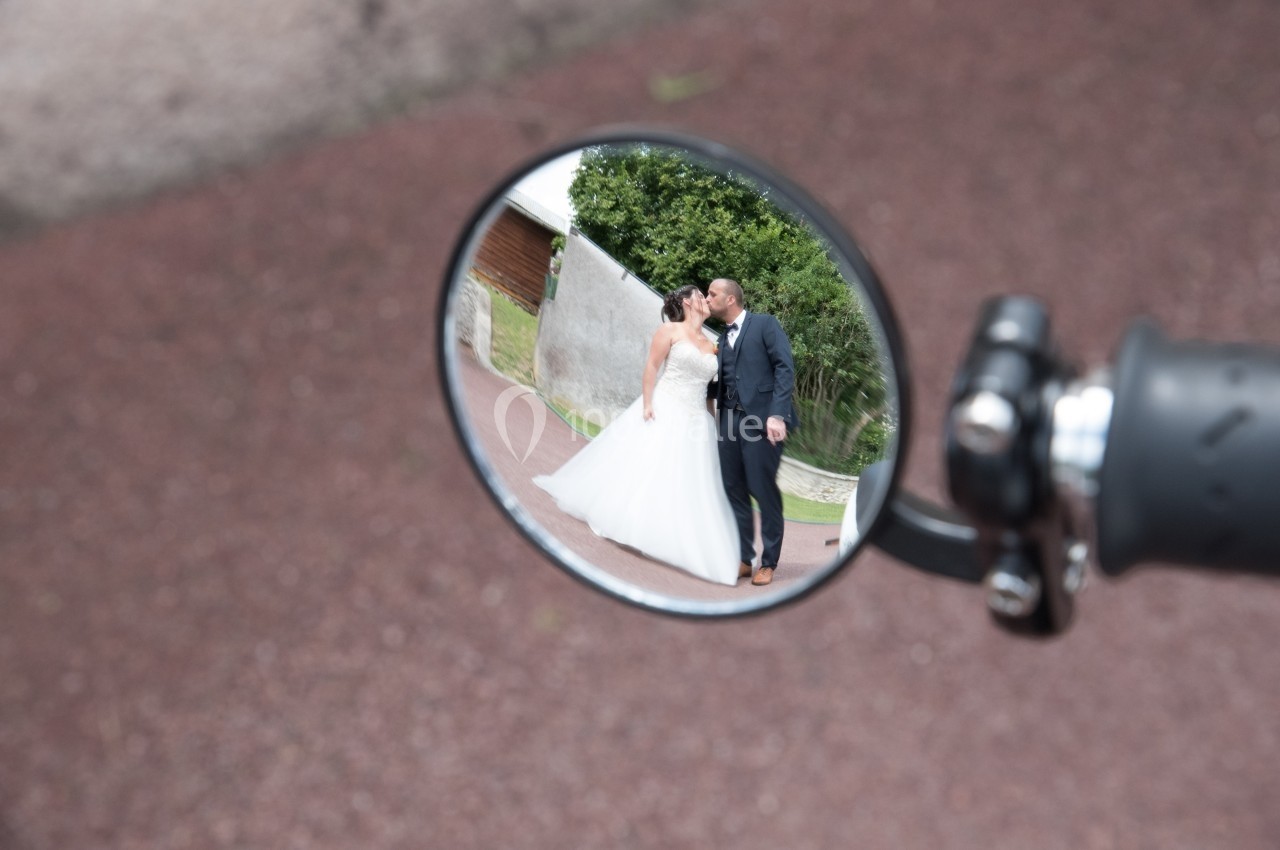 Un couple de mariés s'embrasse, reflété dans le rétroviseur d'une moto sur une route.