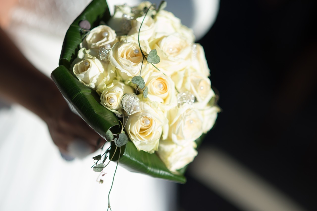 Bouquet de roses blanches et crème entouré de feuilles vertes, tenu par une personne en tenue blanche.