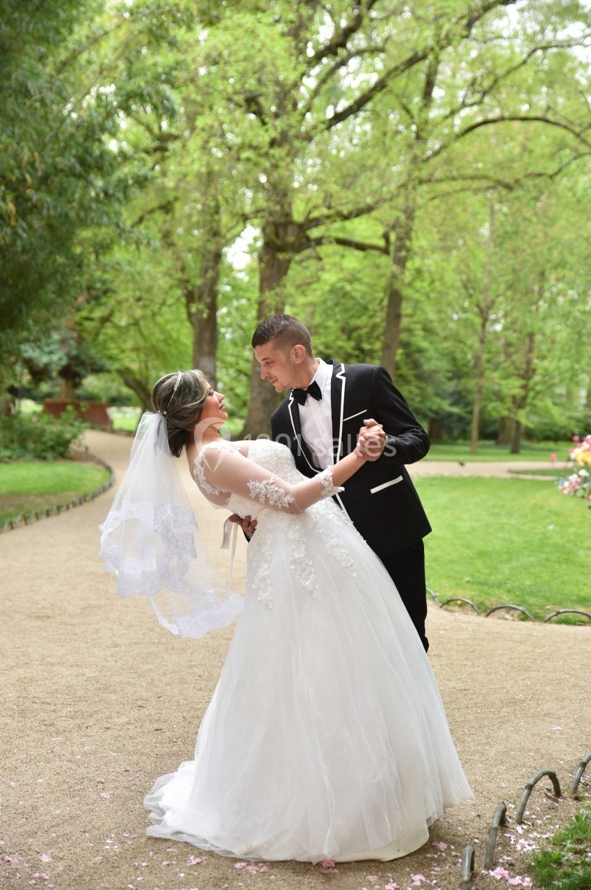 Un couple en tenue de mariage danse dans un parc verdoyant sous des arbres feuillus.