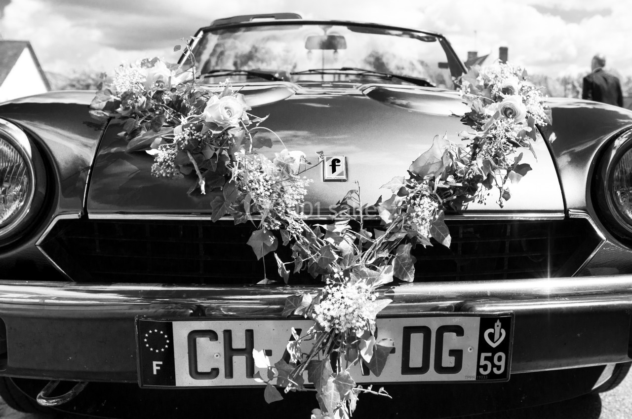 Voiture ancienne décapotable décorée de fleurs pour une cérémonie, stationnée sur une rue pavée.