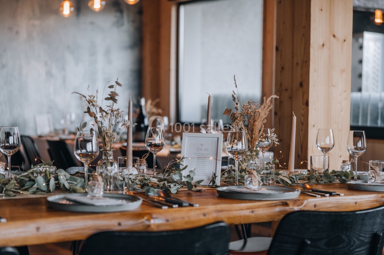 Table en bois décorée avec des bougies, des verres et des arrangements floraux dans un cadre intérieur chaleureux.