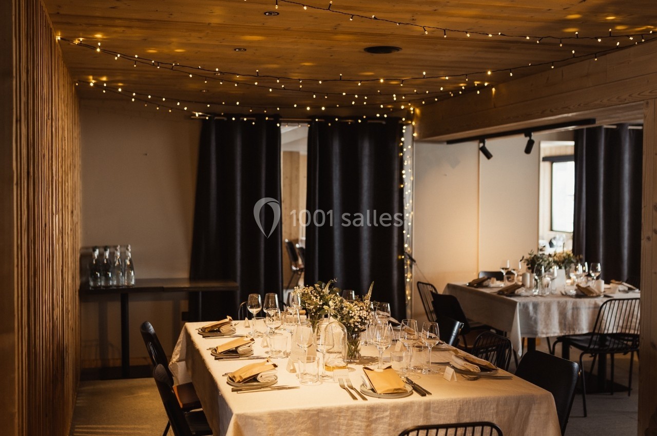 Salle décorée avec des guirlandes lumineuses, tables dressées avec nappes blanches, vaisselle élégante et centres de table…