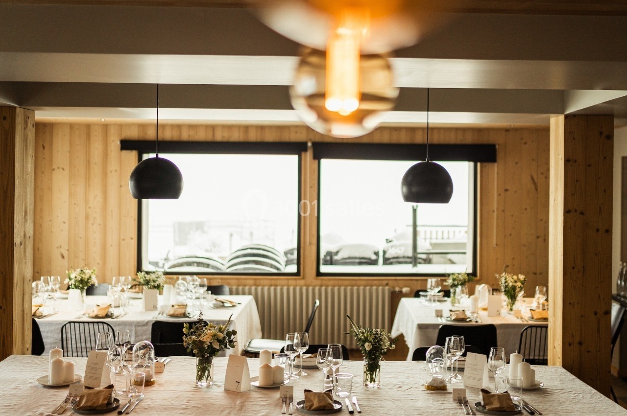 Salle de restaurant lumineuse avec tables dressées, nappes blanches, décorations florales et grandes fenêtres donnant sur l…
