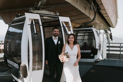 Miniature Location salle La Clusaz (Haute-Savoie) - Le 1647 #4 Un couple en tenue de mariage se tient dans un paysage montagneux au coucher du soleil, entouré de sapins.