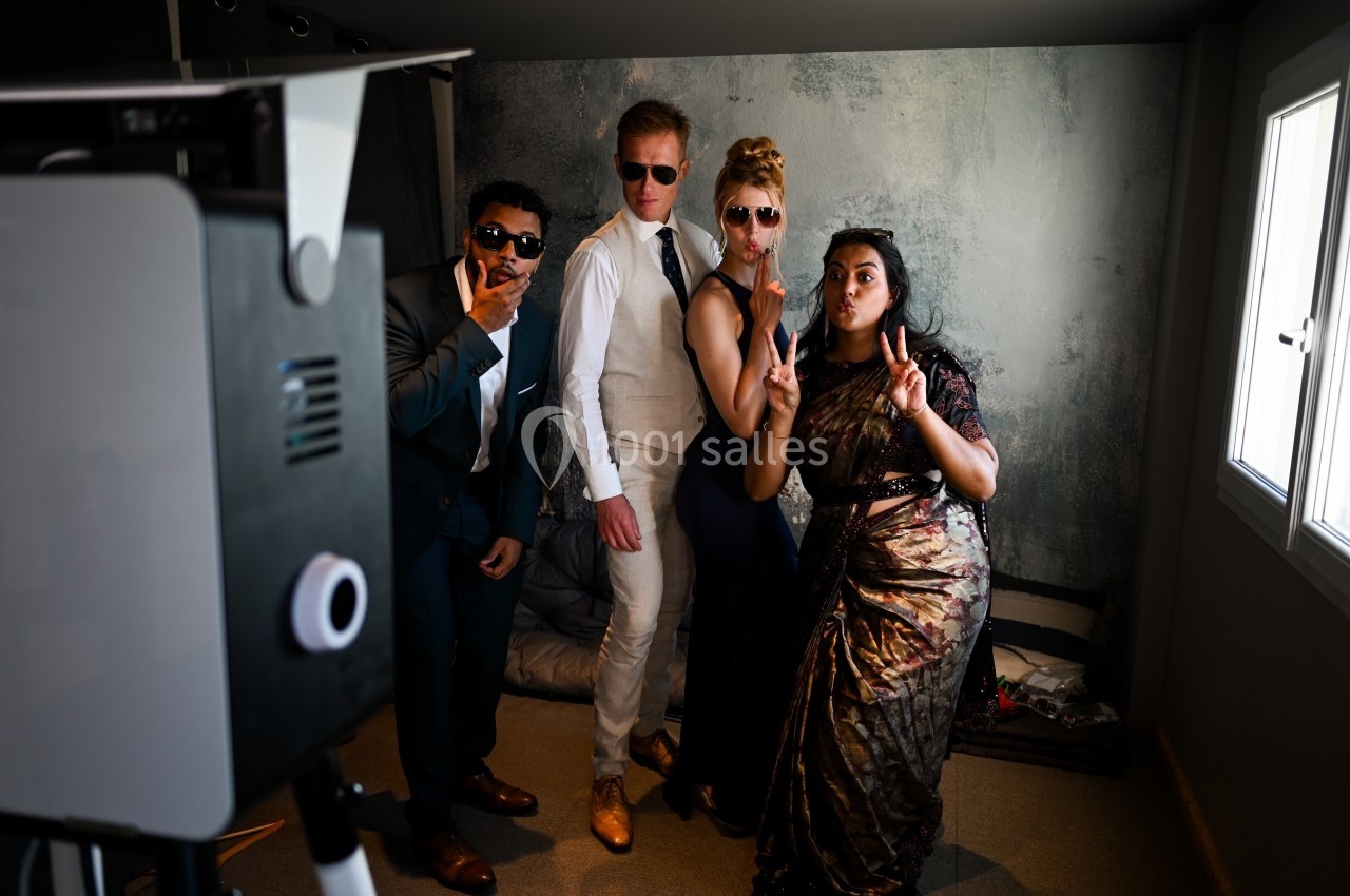 Quatre personnes posent de manière décontractée devant un photobooth, dans une pièce éclairée par une fenêtre.