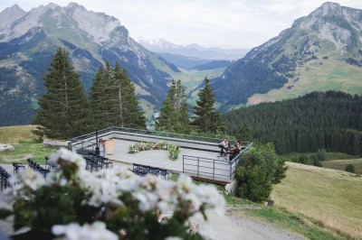 Miniature Location salle La Clusaz (Haute-Savoie) - Le 1647 #17 Un couple en tenue de mariage se tient dans un paysage montagneux au coucher du soleil, entouré de sapins.