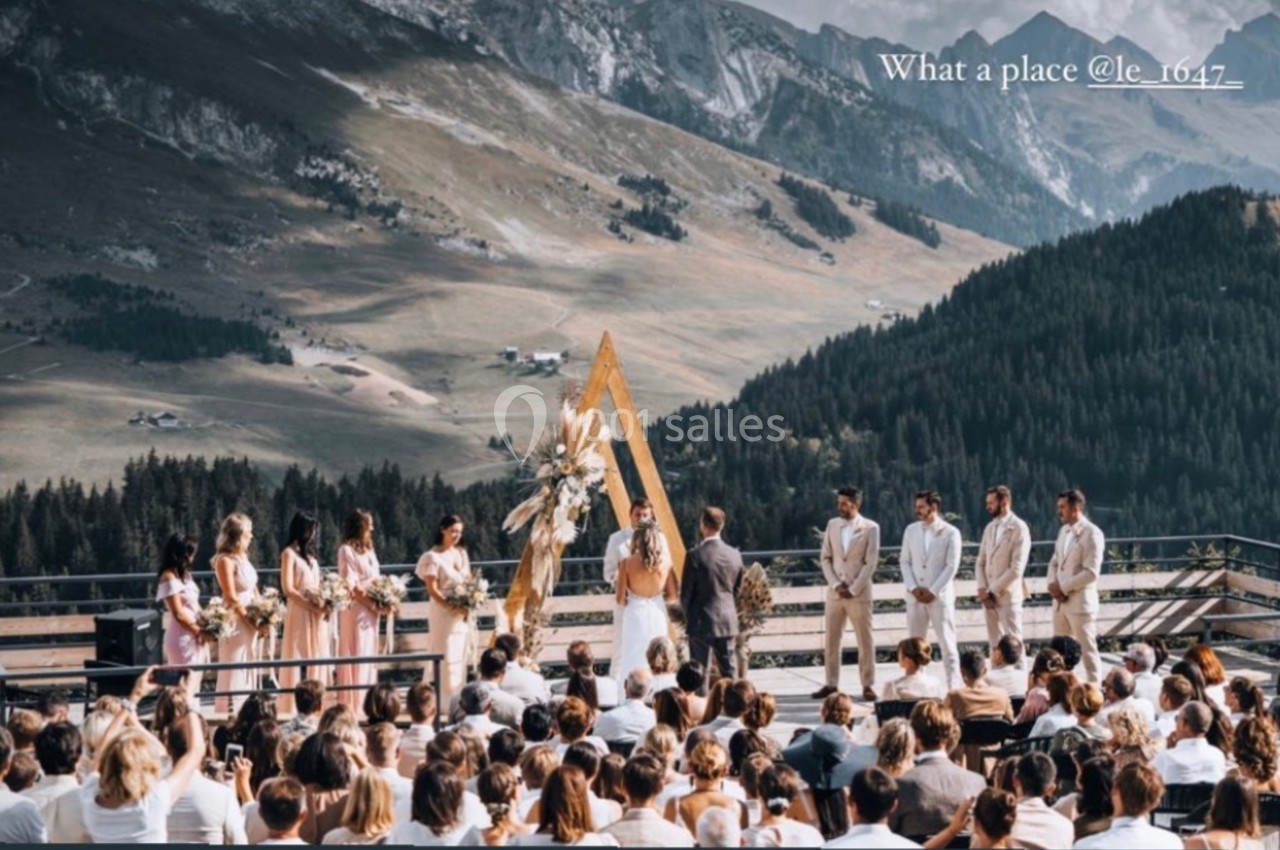 Cérémonie de mariage en plein air avec vue sur des montagnes et une vallée, invités assis face aux mariés.
