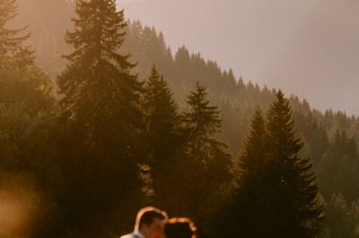 Miniature Location salle La Clusaz (Haute-Savoie) - Le 1647 #20 Un couple en tenue de mariage se tient dans un paysage montagneux au coucher du soleil, entouré de sapins.