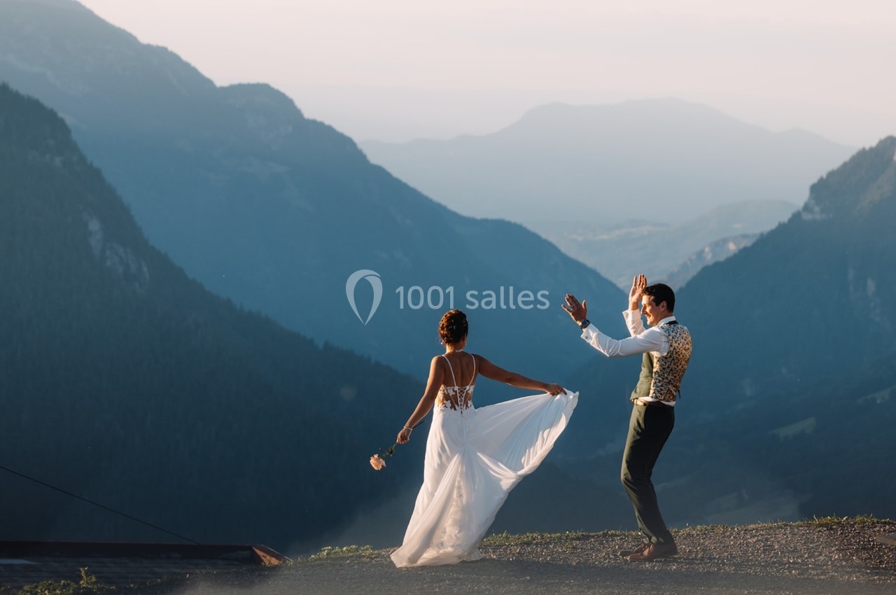 Un couple danse en plein air sur un sommet montagneux, entouré de paysages vallonnés au coucher du soleil.