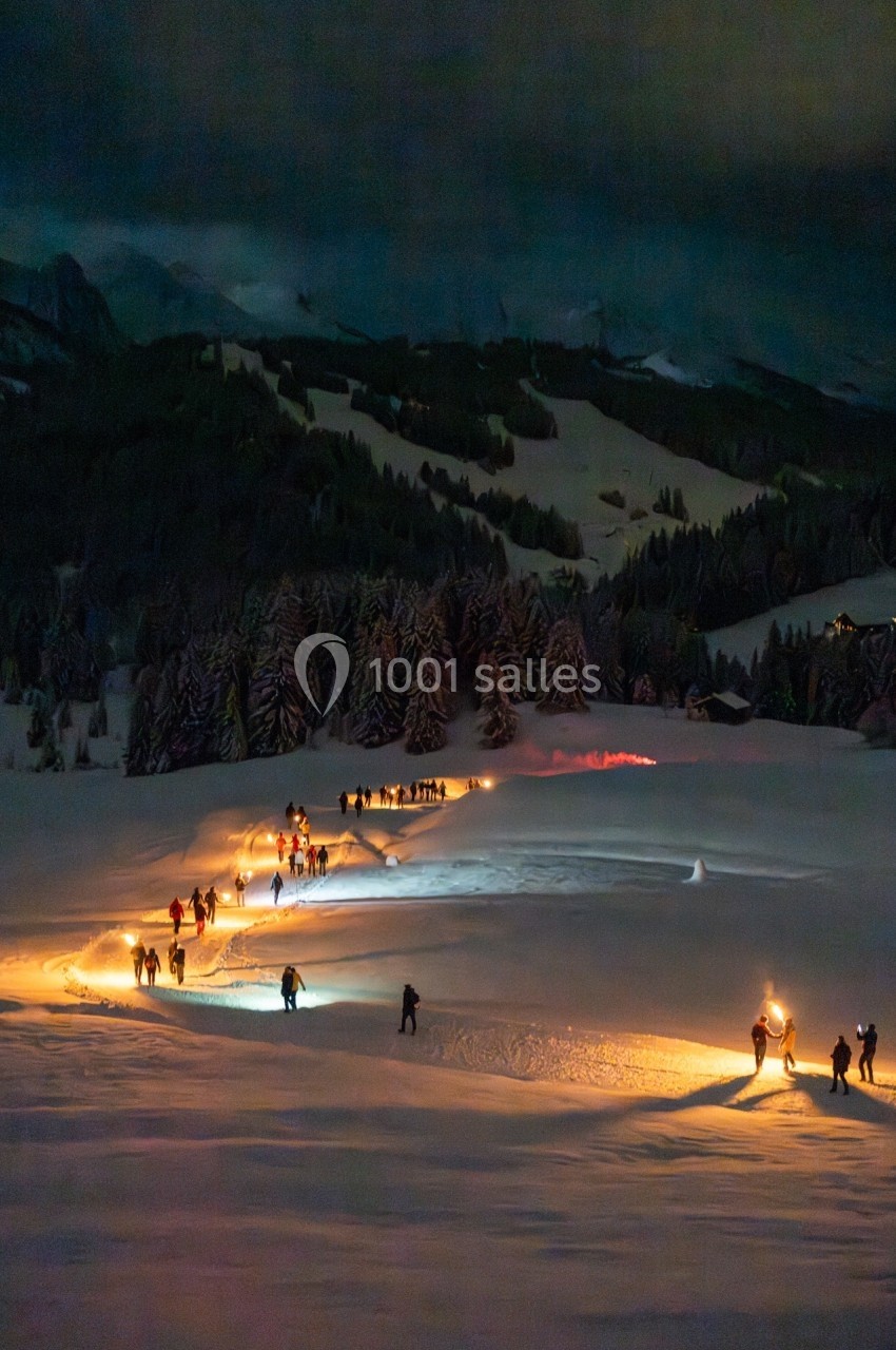 Un groupe de randonneurs marche de nuit dans la neige, éclairé par des torches et des lampes frontales.