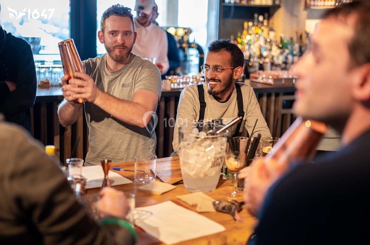 Des personnes participent à un atelier de mixologie dans un bar, préparant des cocktails avec des shakers et des ingrédients…