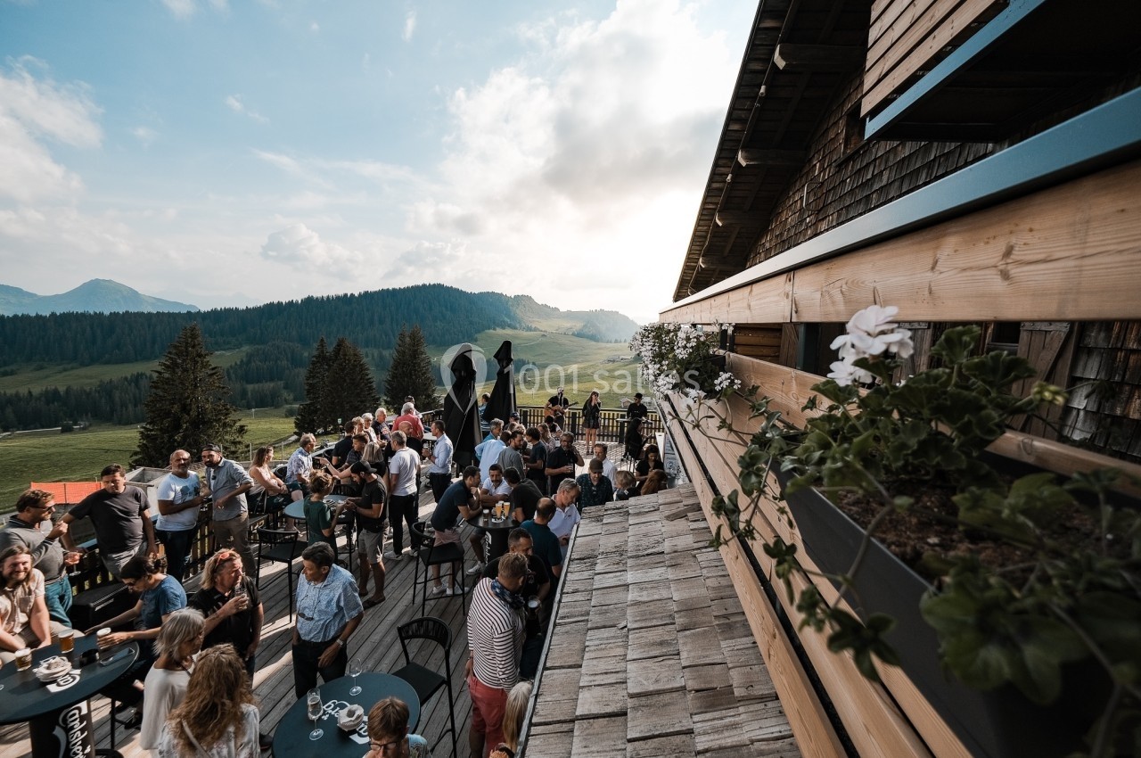Groupe de personnes rassemblées sur une terrasse en bois avec vue sur des montagnes et une vallée verdoyante.