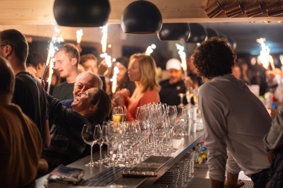 Un DJ mixe sur son ordinateur portable lors d'une soirée animée dans un espace intérieur éclairé par des lumières colorées.
