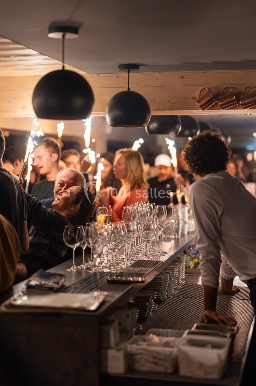 Des personnes rassemblées dans un bar animé, tenant des cierges magiques allumés, avec des verres posés sur le comptoir.