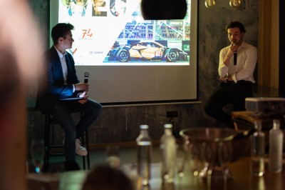 Un DJ mixe sur son ordinateur portable lors d'une soirée animée dans un espace intérieur éclairé par des lumières colorées.