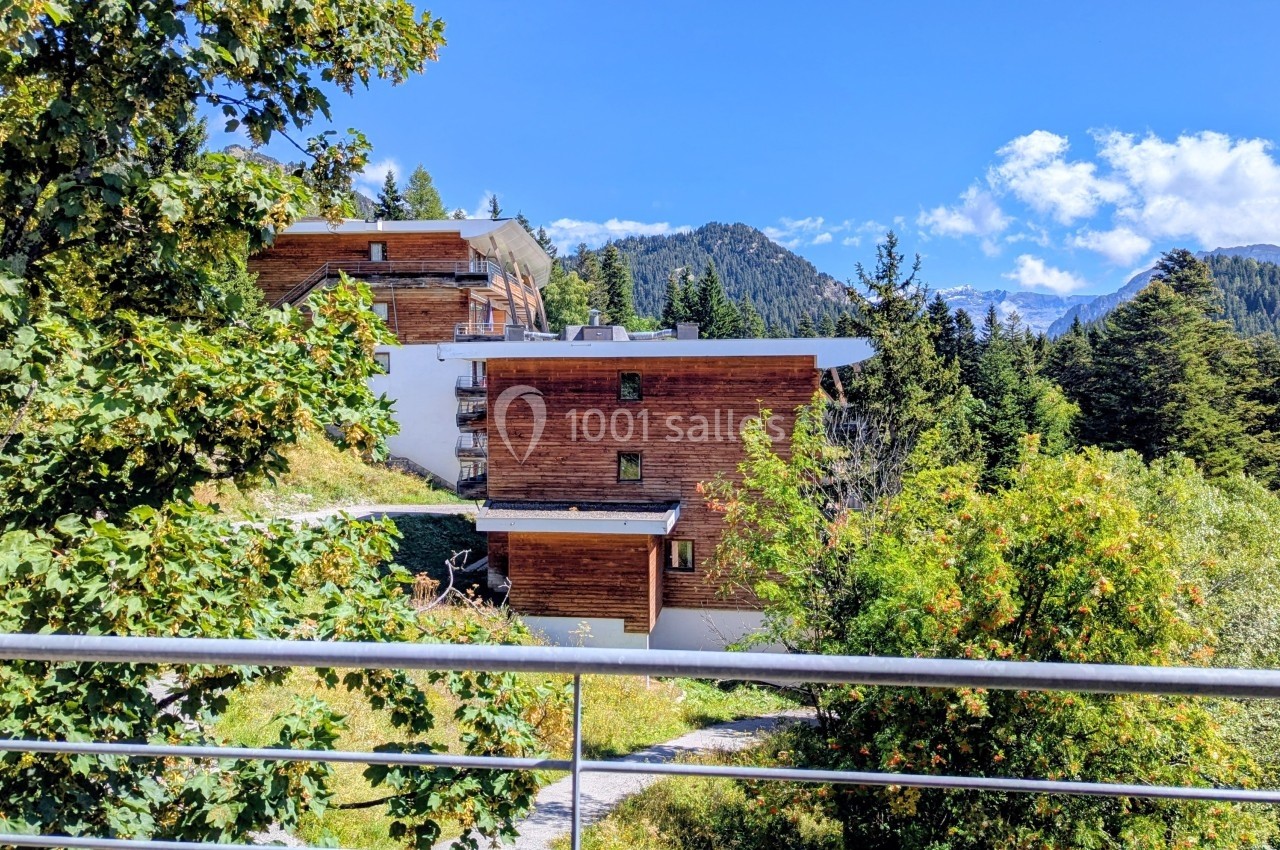 Chalets en bois entourés de végétation alpine, avec vue sur des montagnes sous un ciel bleu dégagé.
