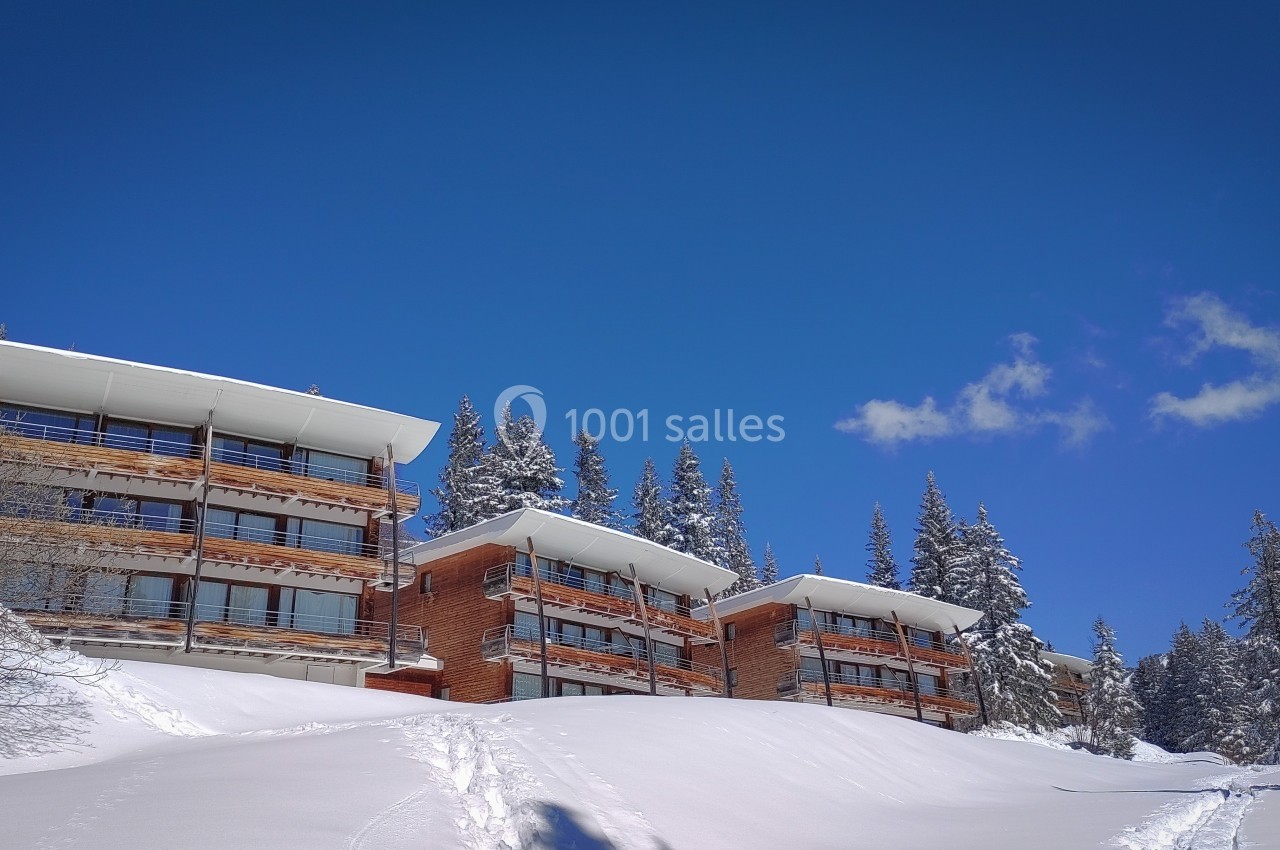 Immeubles en bois entourés de neige et de sapins sous un ciel bleu clair.