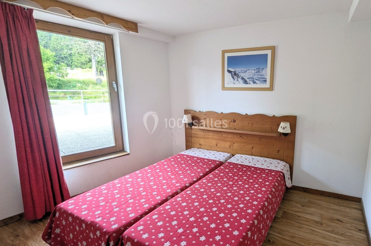 Deux lits simples avec couvre-lits rouges à motifs, une fenêtre donnant sur l'extérieur et un tableau au mur.