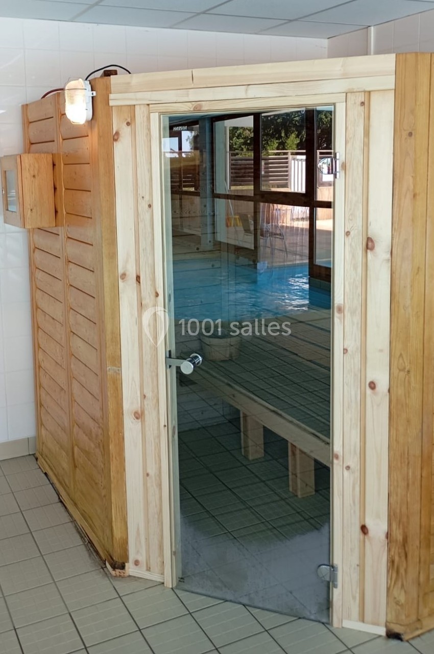Cabine de sauna en bois avec porte vitrée, située dans un espace intérieur carrelé près d'une piscine.