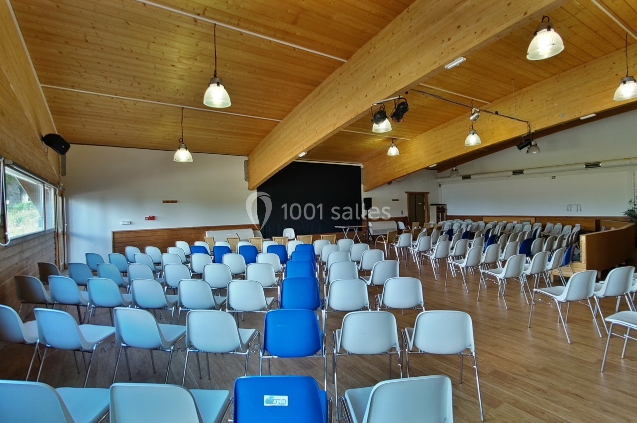 Salle de réunion avec des rangées de chaises blanches et bleues, un écran noir et un plafond en bois éclairé.