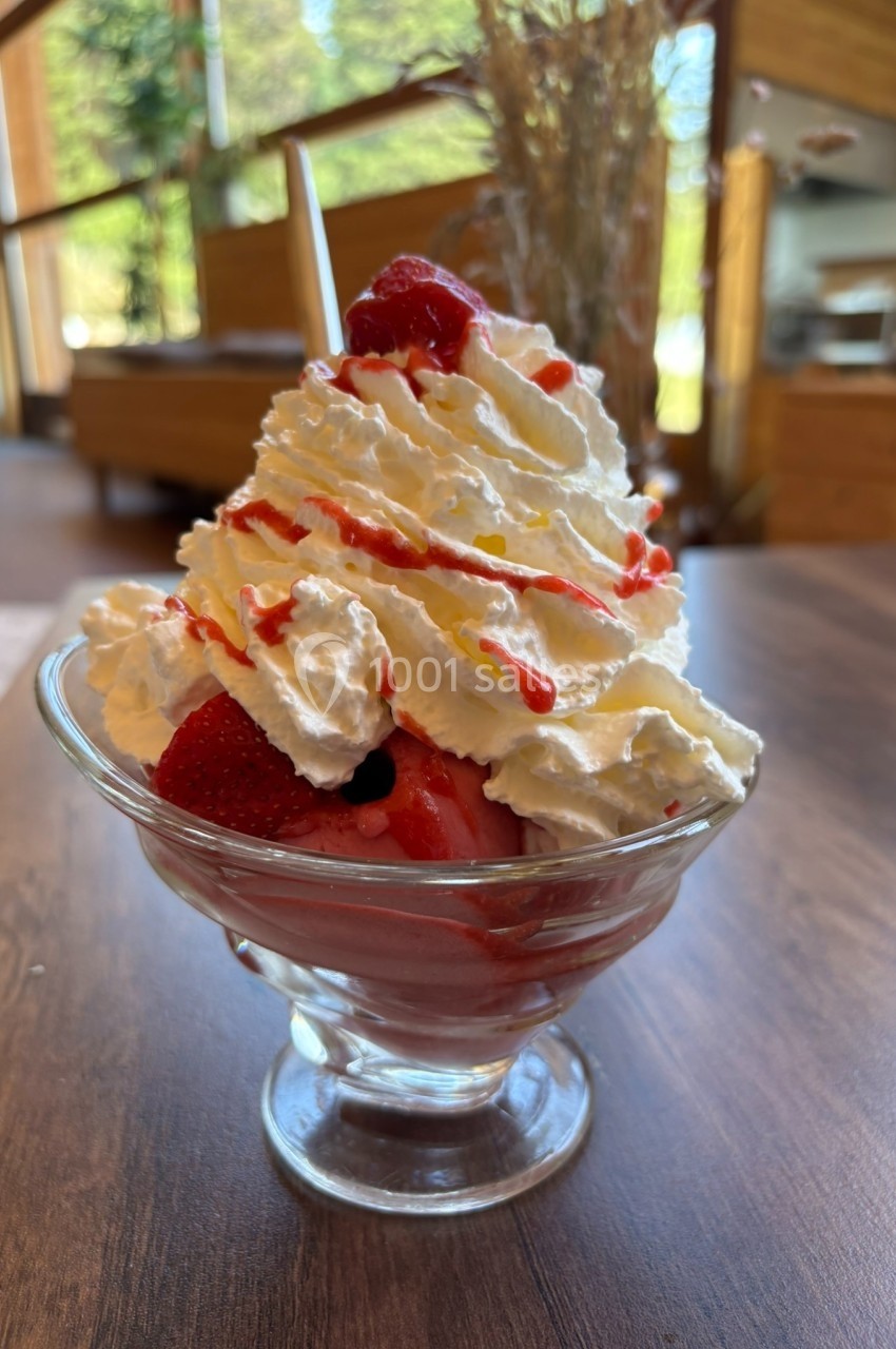 Coupe de fraises fraîches garnie de chantilly et de coulis rouge, servie dans un verre sur une table en bois.