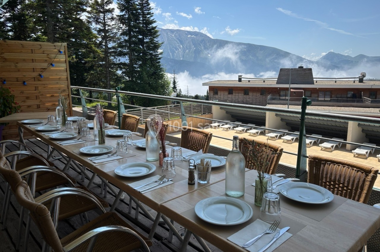 Table dressée en extérieur avec vue sur des montagnes, des sapins et une terrasse ensoleillée.