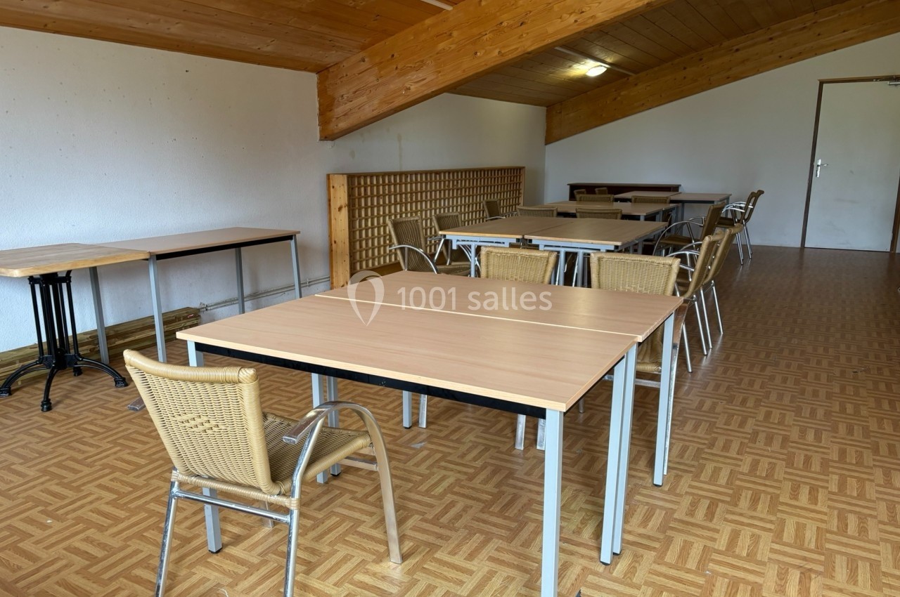 Salle avec des tables en bois clair, des chaises en osier et un plafond en bois incliné.