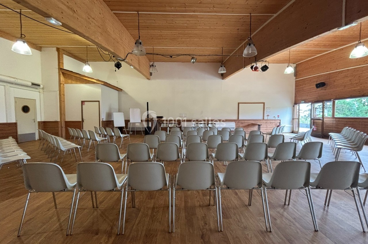 Salle de réunion avec des rangées de chaises blanches vides, un tableau blanc et un plafond en bois.