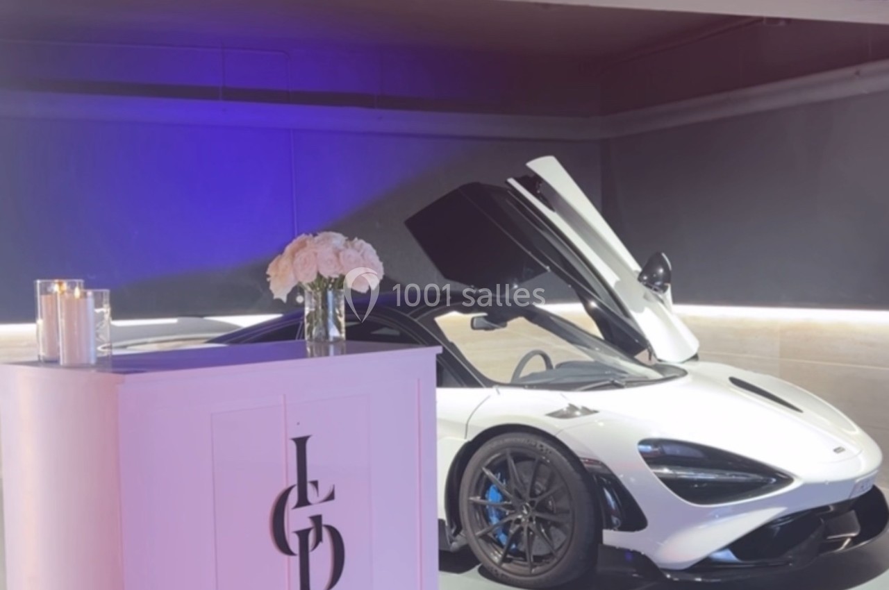 Voiture de sport blanche aux portes ouvertes exposée dans un espace moderne avec éclairage tamisé et décor minimaliste.