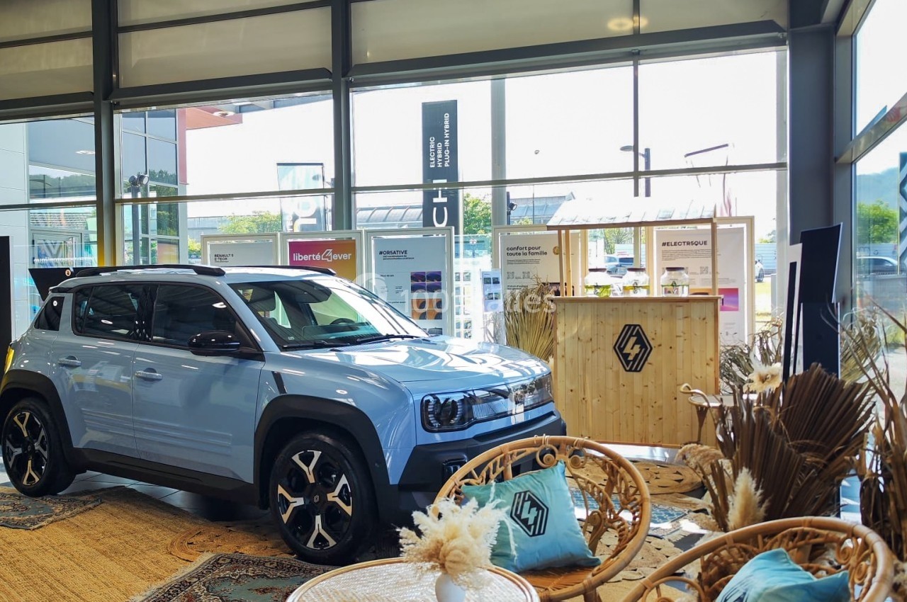 Un SUV bleu exposé dans un showroom lumineux, entouré de fauteuils en rotin et de décorations bohèmes.