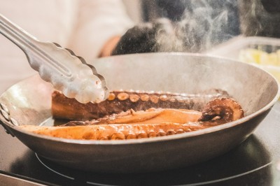 Tentacules de poulpe en train de cuire dans une poêle, manipulés avec une pince en métal.