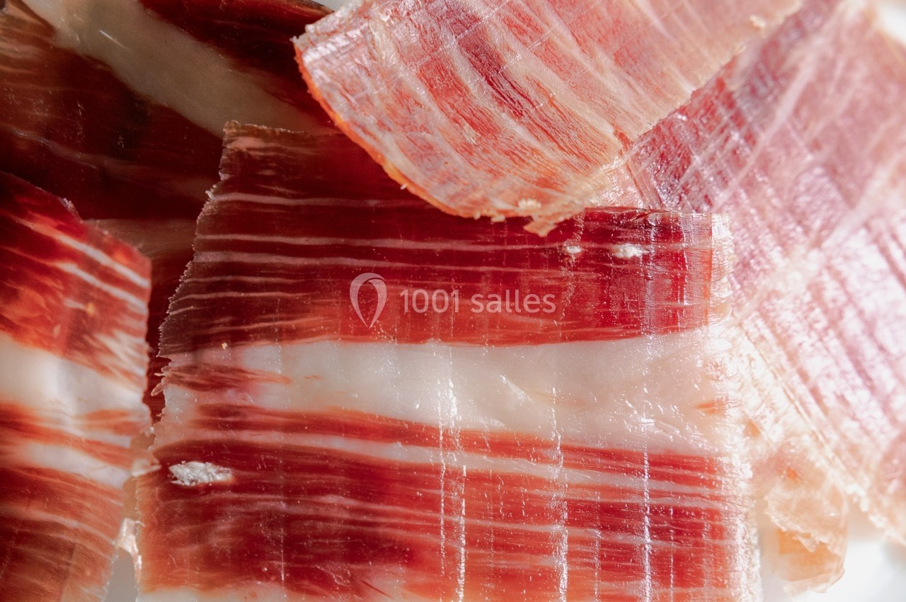Tranches fines de jambon cru avec des marbrures de gras blanc sur fond neutre.