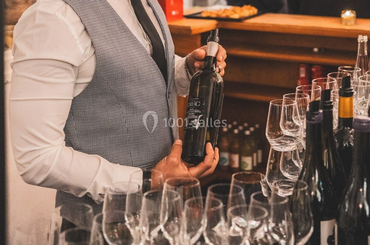 Un serveur en gilet présente une bouteille de vin derrière un comptoir avec des verres disposés.