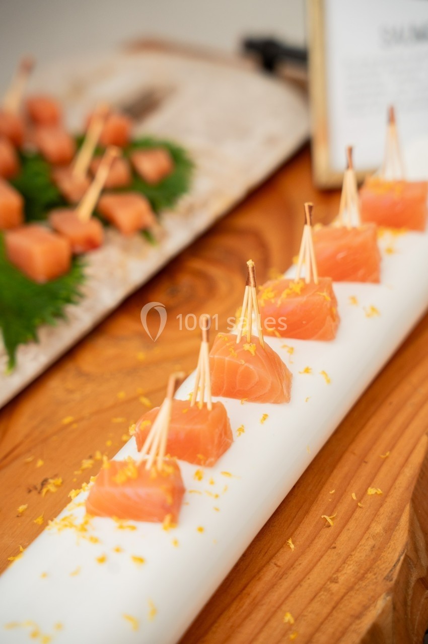 Dés de saumon frais sur des piques en bois, présentés sur un support blanc avec des zestes d'agrumes.
