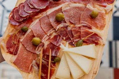 Planche en bois garnie de charcuteries, tranches de fromage et olives vertes, posée sur un sol carrelé coloré.