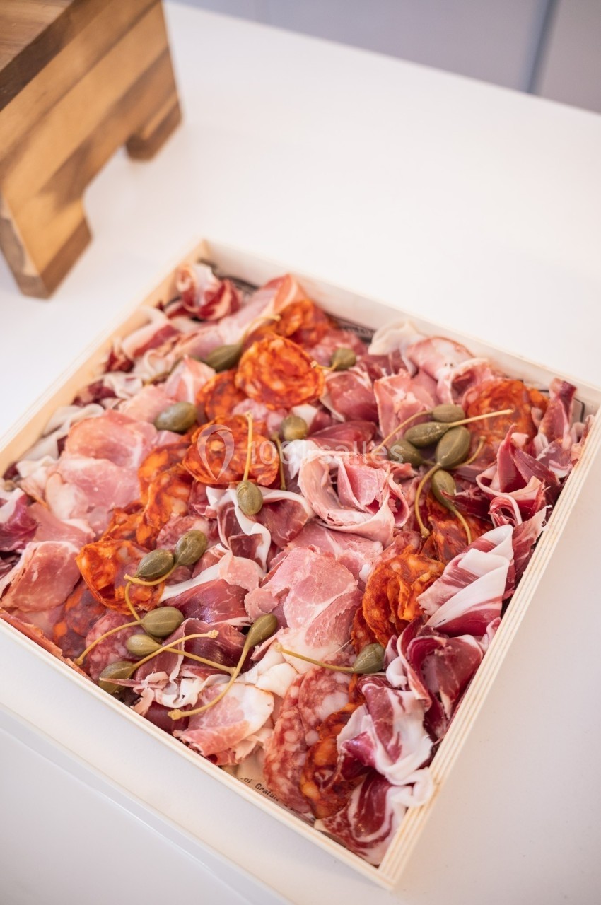 Plateau en bois garni de charcuteries variées, dont jambon, chorizo et salami, décoré de câpres.