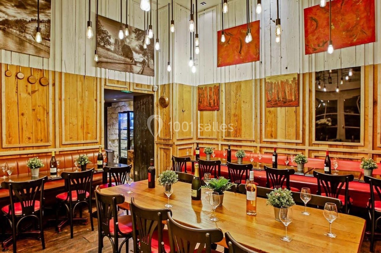 Salle de restaurant chaleureuse avec murs en bois, tables dressées, chaises noires et décorations murales colorées.